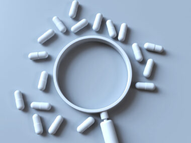 A magnifying glass is surrounded by a scattering of pills.