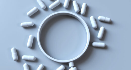 A magnifying glass is surrounded by a scattering of pills.
