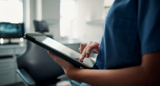 A healthcare professional, shown from the chest to the waist, uses a tablet.