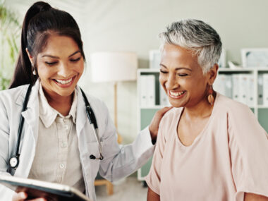 A doctor and a patient smile as they look at a tablet.
