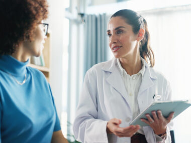 A doctor holds a tablet while speaking with a patient.