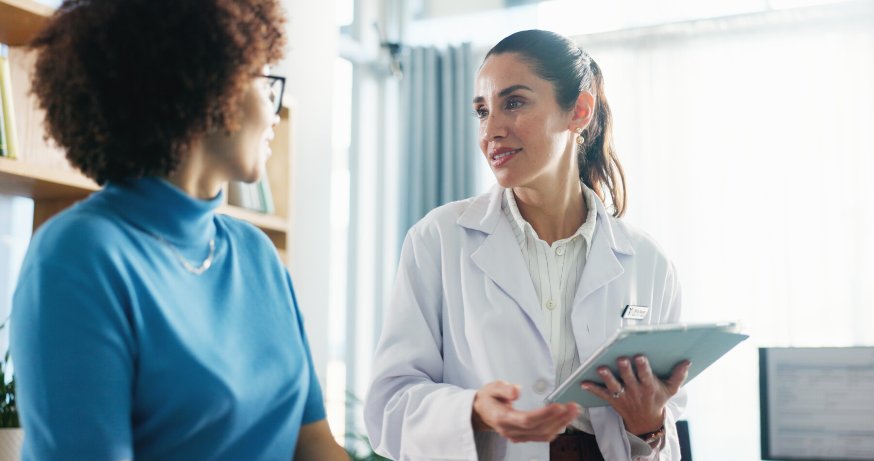 A doctor holds a tablet while speaking with a patient.