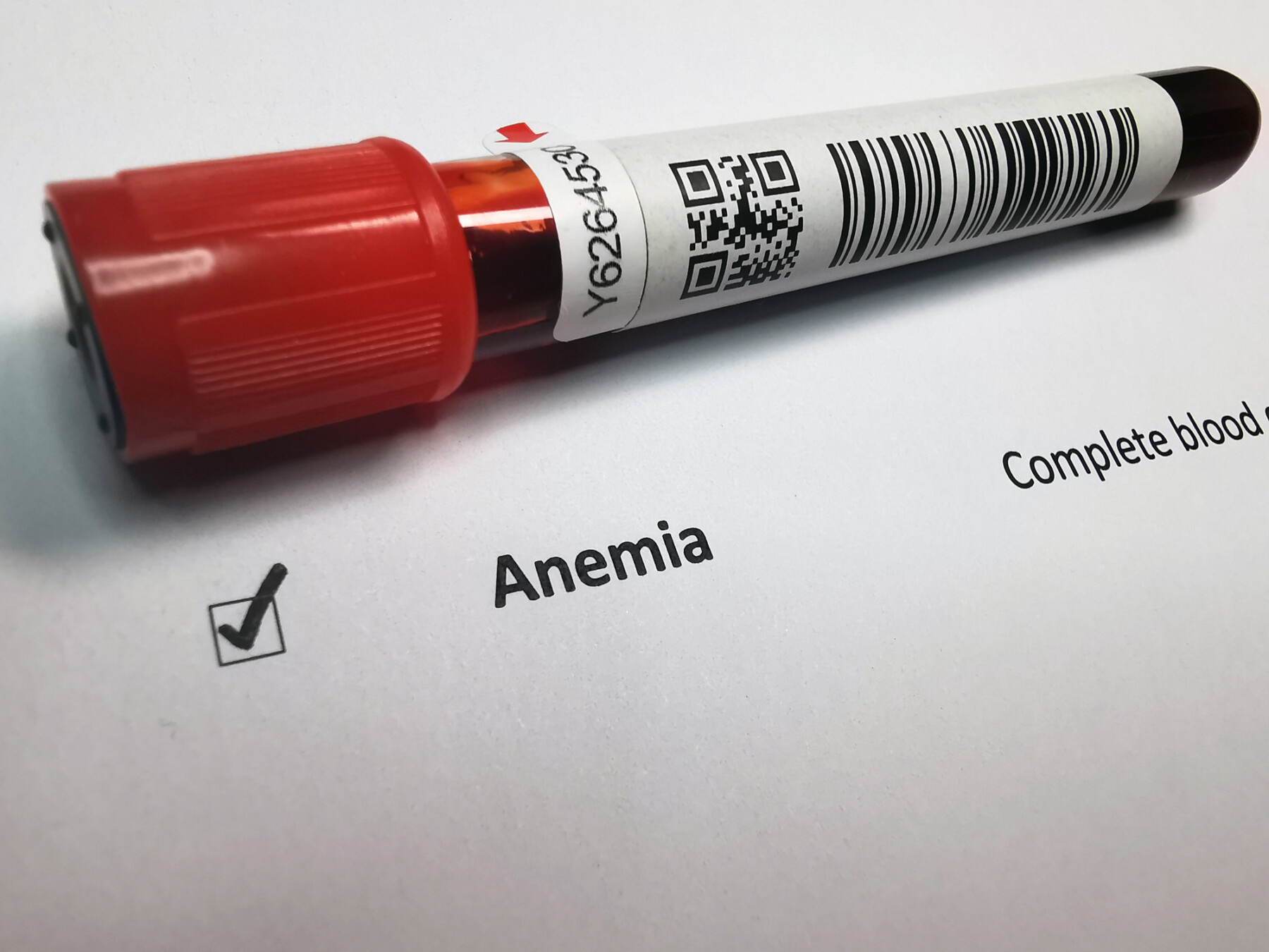A vial of labeled blood sits on a sheet of paper that shows a checked box indicating anemia.